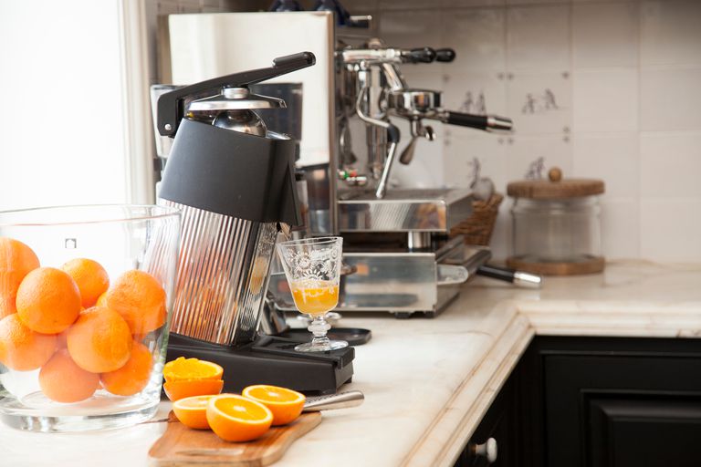 Freshly cut oranges being used to make orange juice and an espresso machine in the background.
